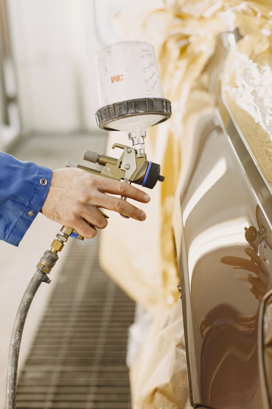 Pintura automotiva sendo aplicada com pistola em cabine de pintura